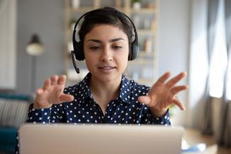 Young woman wearing wireless headset video calling on laptop